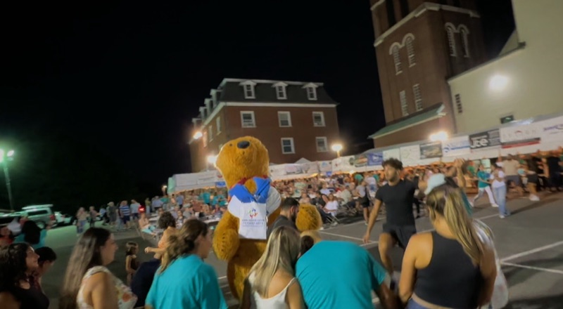 Bear mascot greeting the crowd at an evening community street event